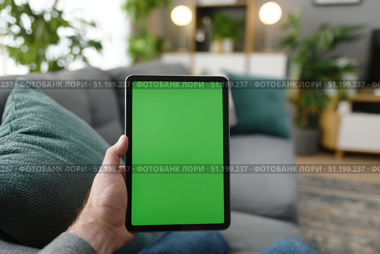 Young person holding a digital tablet with green screen in a dining room. Computer Mockup. Person using digital tablet green background display. Chroma key device. Closeup. Personal view. POV. Стоковое AI-изображение, AI-художник Марина Демидюк / Фотобанк Лори