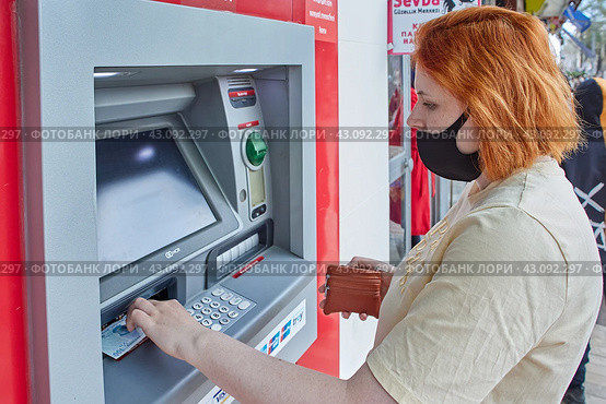 Young white woman wearing PPE gets cash in form of paper currency at street ATM. (2021 год). Редакционное фото, фотограф Владимир Григорьев / Фотобанк Лори