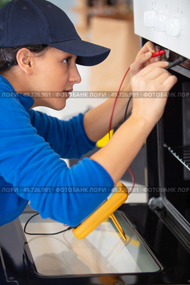 young woman checks oven malfunction with multimeter. Стоковое фото, агентство Ingram Publishing / Фотобанк Лори