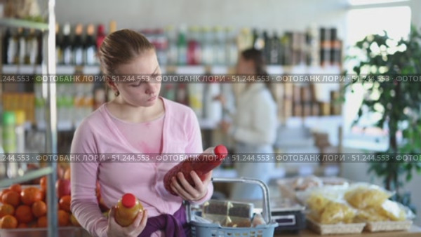 Young woman chooses freshly squeezed tomato and peach juice in glass bottles in a supermarket against the backdrop of buyers. Стоковое видео, видеограф Яков Филимонов / Фотобанк Лори
