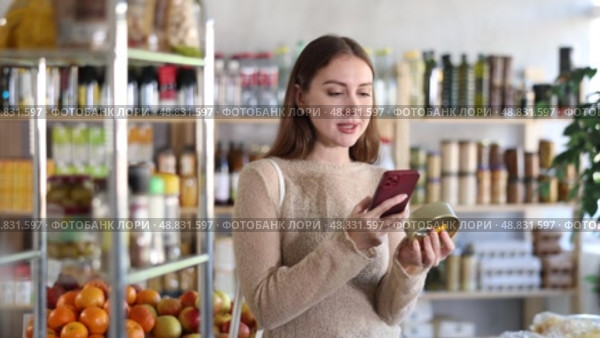 Young woman customer at shop scans QR code on tin cans of preserves using phone camera. Стоковое видео, видеограф Яков Филимонов / Фотобанк Лори