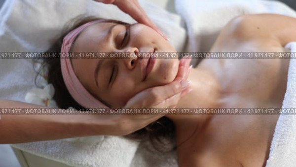 Young woman enjoying professional facial massage to relieve muscle tension and improve skin elasticity and firmness in beauty salon. Стоковое видео, видеограф Яков Филимонов / Фотобанк Лори