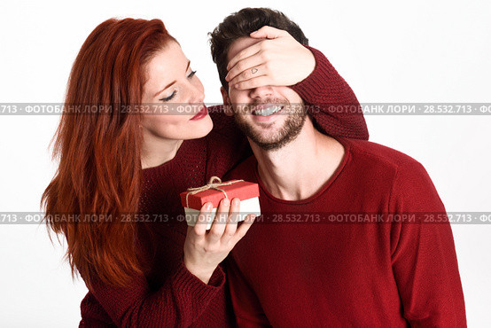 Young woman giving a gift to his man. Beautiful couple dressed in red on white background. Redhead girl. Стоковое фото, фотограф Javier Sánchez Mingorance / Ingram Publishing / Фотобанк Лори