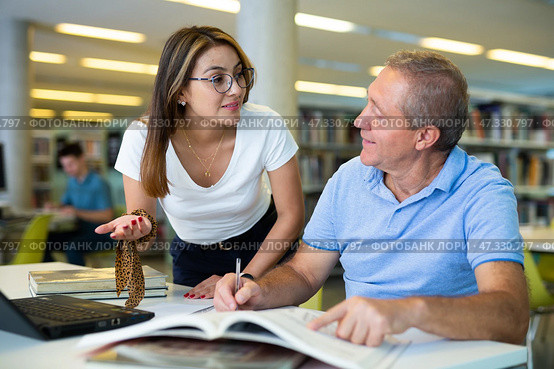 Young woman librarian helps an elderly man find the necessary information in laptop. Стоковое фото, фотограф Яков Филимонов / Фотобанк Лори