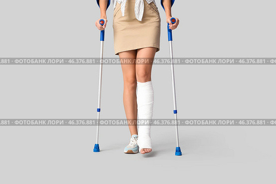 Young woman with broken leg and crutches on light background. Стоковое фото, фотограф Pixel_shot / Фотобанк Лори