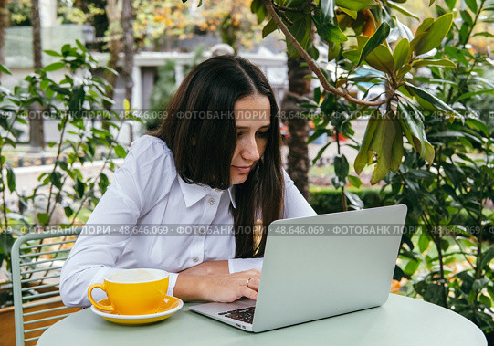 Young woman works with laptop on terrace of  cafe. Hunched posture, professional spinal deformity concept. Стоковое фото, фотограф Алена Аксенова / Фотобанк Лори