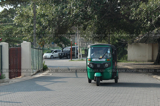 Зеленый тук-тук едет по тихой улице днем ​​в Галле, Шри-Ланка.  Green Tuk-Tuk Driving Down Quiet Street in Daylight in Galle, Sri Lanka (2018 год). Редакционное фото, фотограф Соболева Наталия / Фотобанк Лори