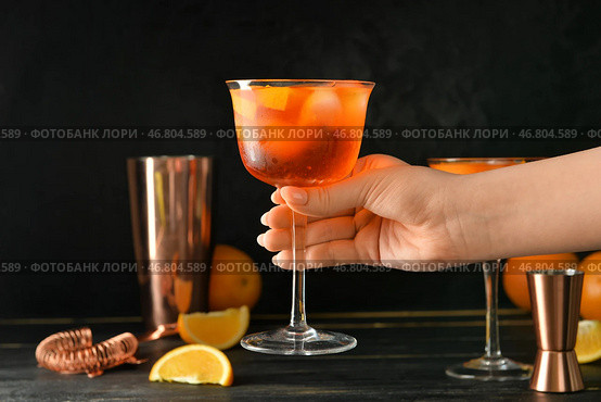 Женщина держит стакан вкусного коктейля aperol spritz на темном фоне, крупным планом. Стоковое фото, фотограф Pixel_shot / Фотобанк Лори