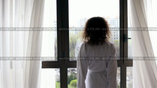 Женщина в банном халате подходит к окну, раздвигает шторы и смотрит на улицу. Стоковое видео, видеограф Losevsky Pavel / Фотобанк Лори