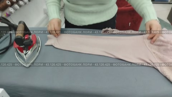 Женщина в швейном ателье гладит утюгом на гладильной доске кофту. A woman in a sewing studio irons a jacket on an ironing board. Стоковое видео, видеограф Наталья Пеньшина / Фотобанк Лори