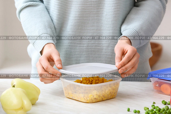 Женщина закрывает пластиковый контейнер с кукурузой на кухне, крупным планом. Стоковое фото, фотограф Pixel_shot / Фотобанк Лори