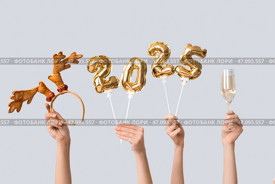 Женские руки с фигурками 2025 из воздушных шаров из фольги, бокал шампанского и ободок с рогами на белом фоне. Стоковое фото, фотограф Pixel_shot / Фотобанк Лори