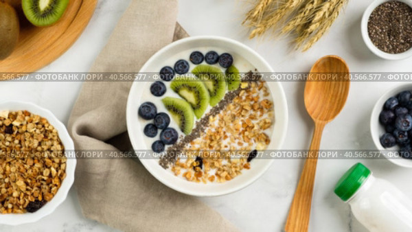 Zoom in healthy breakfast consisting of natural yogurt with granola, kiwi fruit, chia seeds and blueberries, top view. Concept of healthy food, vegetarian eating. Стоковое видео, видеограф Мария Зубарева / Фотобанк Лори